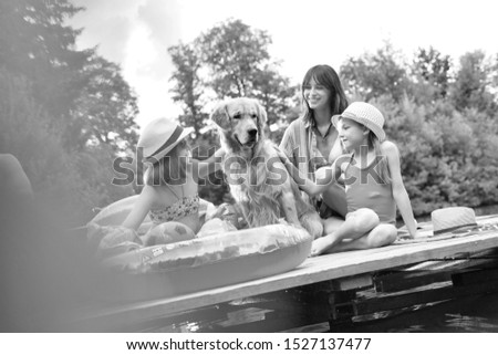 Black and white photo of Mother and daughter stroking golden retriever on pier during summer weekend