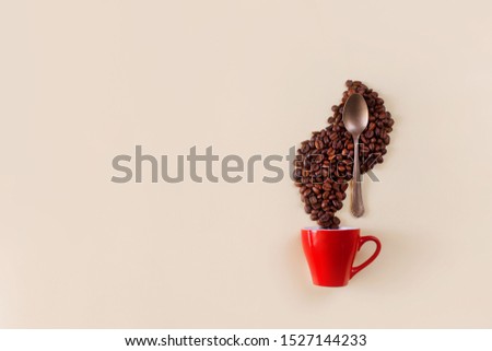 Creative still life with red coffee cup, spoon and roasted coffee beans. Coffee beans rise above a cup in the shape of a steam. Flat lay with hot drink on a beige background. Minimalism, copy space.