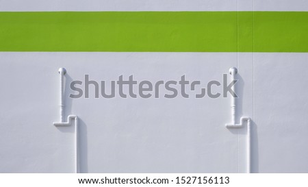 Front view of 2 protective white PVC corrugated pipes with electrical cables inside on white cement wall with green stripe background outside of building