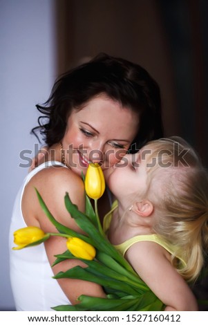 
Happy mother's day daughter congratulates mom kisses on the cheek and gives a bouquet of yellow tulips. Happy and smiling mom and daughter - Image