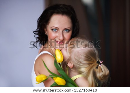 Happy mother's day daughter congratulates mom kisses on the cheek and gives a bouquet of yellow tulips. Mom is looking at the camera. Happy mom and daughter - Image