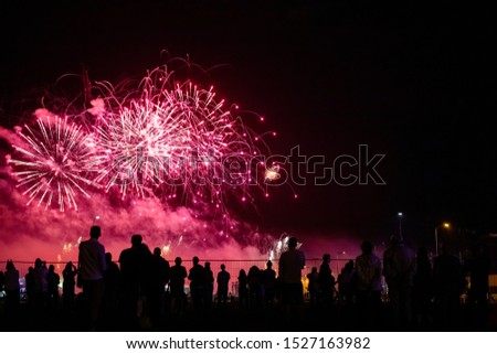 silhouettes of people watching fireworks in the background of bright red flashes in the night sky