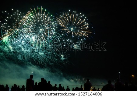 silhouettes of people watching fireworks in the background of bright red flashes in the night sky