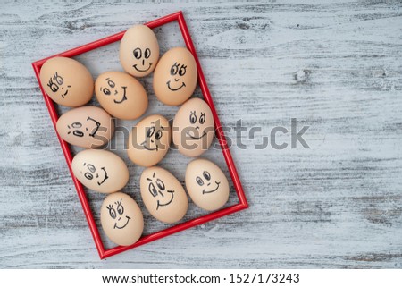 Picture red frame and many funny eggs smiling on white wooden wall background, close up. Eggs family emotion face portrait. Concept funny food. Copy space