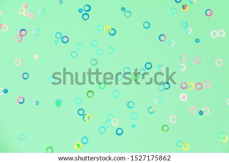 Colorful holographic foil confetti background. Pastel colored pink, blue and yellow circles sparse on trendy neo mint green colored paper. Simple holiday concept. Top view, flat lay Year color trend