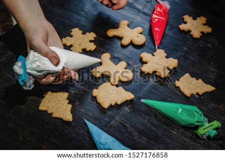 decorate Christmas gingerbread cookies using colored glaze on a dark wooden table, top view
