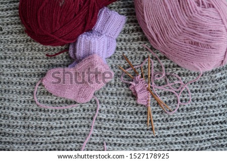 Knitting soft woolen baby socks, light pink and purple, on chunky knitted background