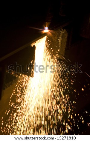 Sparks flying during cutting of a sheet of steel at a factory workshop.