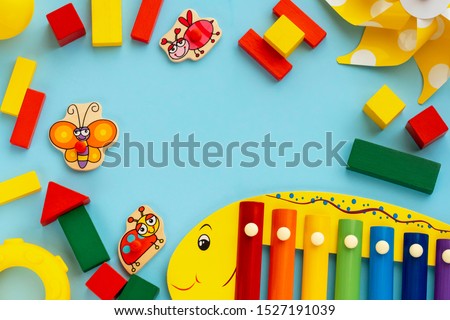 Top view on children's educational and music games, frame from multicolored kids toys on light blue paper background. Wooden cubes, stars, circles, ladybag, pinwheel, xylophone, cute butterfly. Flat Royalty-Free Stock Photo #1527191039
