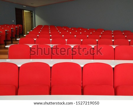 Amphitheater big lecture room with red chairs and white tables for students lined in rows for university or conference lectures with doors in background