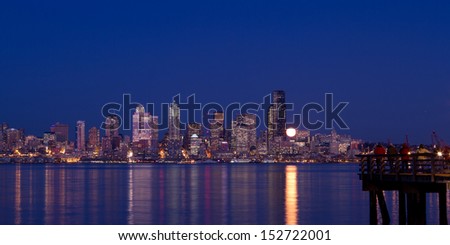 Seattle skyline as seen across Puget Sound at Blue Hour with full moon rising.