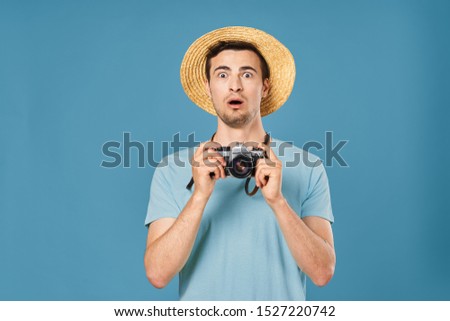 A surprised photographer in a straw hat looks at the camera and holds a camera in his hand