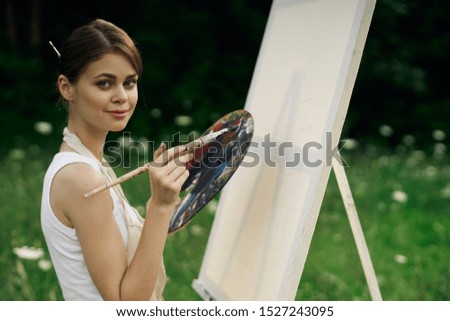 young woman with a brush paints a picture on nature