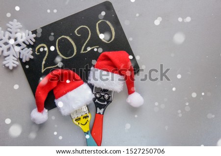 Funny christmas couple brushes with santa hats over grey background and black board with 2020