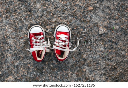 Baby sneakers with white shoelace on grey asphalt background