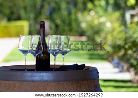Wine bottle and four glasses on the wooden barrel. Welcome drink in winery shop. Wine restaurant outdoor terrace. 