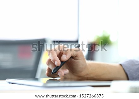 Focus on male hand holding stylos and pointing on tablet screen. Man designer creating new biz project. Business start-up concept. Office interior on blurred background