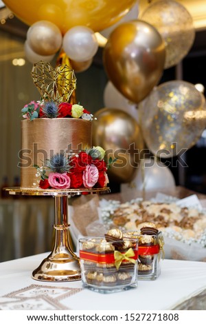 Colourful golden birthday cake with roses and helium balloons as background.