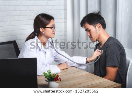Young Asian female doctor examining young man patient. Woman doctor examining man by stethoscope in clinic. Healthcare and medical concept