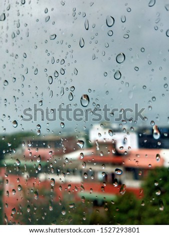 City view through a window on a rainy day, black and white photo. Rain in city in background. RainDrops on green glass background in rainy day. Raindrops on the windshield in the evening. Raindrops 