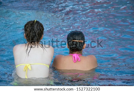 Young women friends talking in water. Two girls sitting in a swimming pool.