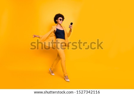 Full length profile side photo of positive afro american have spectacles weekend go use smartphone type sms on social network wear style outfit pants high-heels isolated yellow color background