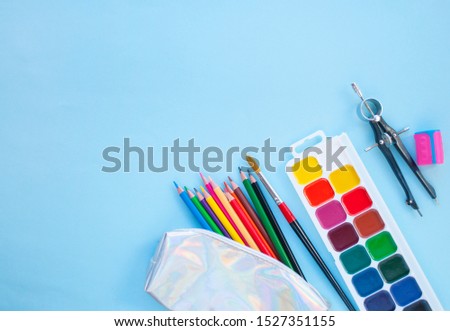 Colorful pencils, watercolors, holographic pencil box on blue background with copyspace. Flat lay style. Back to school concept.