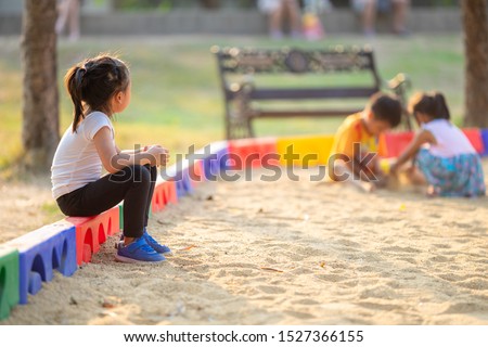 Little girl sitting lonely watching friends play at the playground.The feeling was overlooked by other people.Concept child shy. Royalty-Free Stock Photo #1527366155