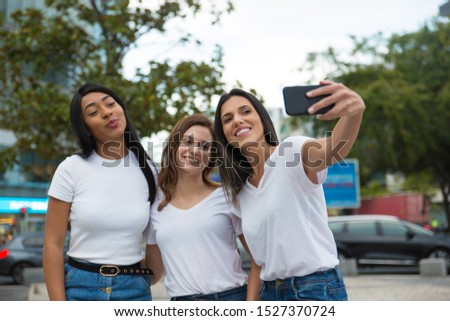 Front view of smiling women posing for selfie on street. Cheerful young ladies taking selfie with smartphone. Concept of self portrait