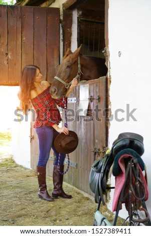          Cowgirl looking at her horse in a barn                             
