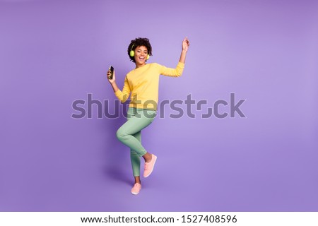 Full length body size photo of trendy stylish cute free girlfriend wearing green pants trousers yellow sweater footwear in headphones listening to music dancing isolated violet pastel color background Royalty-Free Stock Photo #1527408596
