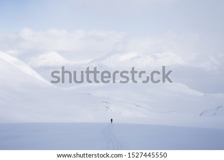 A horizontal shot of a male standing in a snowy area with a lot of high mountains covered with snow