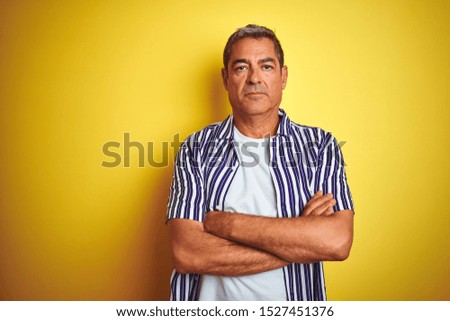 Handsome middle age man wearing striped shirt standing over isolated yellow background skeptic and nervous, disapproving expression on face with crossed arms. Negative person.