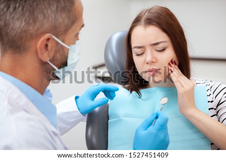 Young woman having toothache, sitting in a dental chair at the clinic. Female patient with terrible toothache visiting dentist Royalty-Free Stock Photo #1527451409