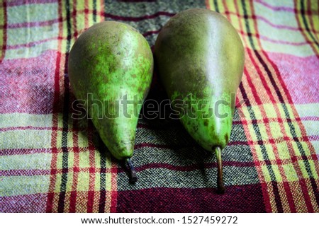 On a checkered colored tablecloth lie two fresh green pears