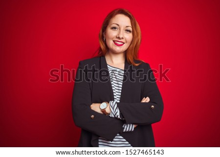 Beautiful redhead business woman wearing elegant jacket over isolated red background happy face smiling with crossed arms looking at the camera. Positive person.