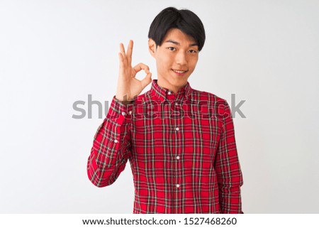 Young chinese man wearing casual red shirt standing over isolated white background smiling positive doing ok sign with hand and fingers. Successful expression.