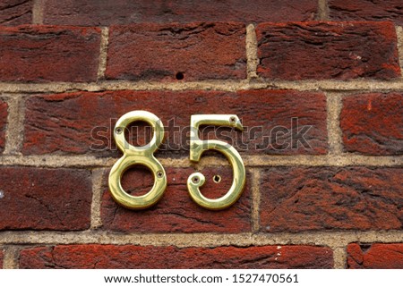House number 85 with golden metal digits on a red brick wall