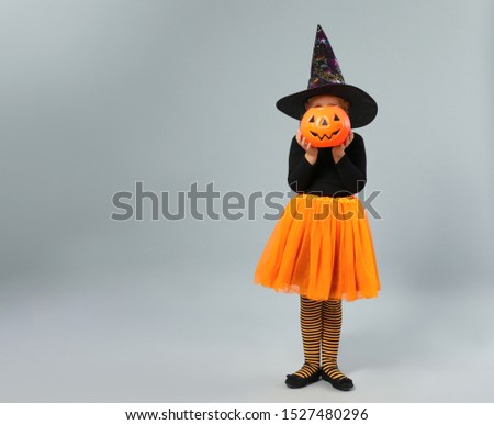 Cute little girl with pumpkin candy bucket wearing Halloween costume on grey background, space for text