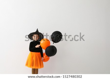 Cute little girl with balloons wearing Halloween costume on light background. Space for text