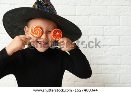 Cute little girl with candies wearing Halloween costume near white brick wall. Space for text