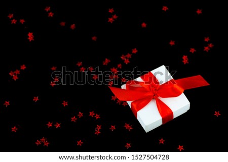 White gift box with a red ribbon and a scattering of stars on a black background.