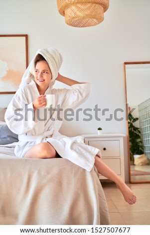 Picture of beatiful girl in white bathrobe with mug of coffee in her hands lying on bed.
