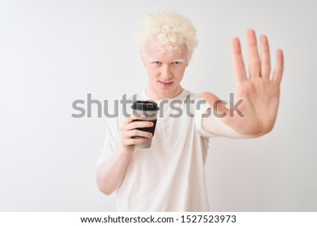 Young albino blond man drinking coffee standing over isolated white background with open hand doing stop sign with serious and confident expression, defense gesture