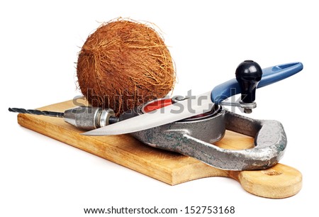 Raw coconut on a cutting board. A knife and a drill. A tool for opening the nut