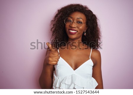 Young african american woman wearing glasses standing over isolated pink background doing happy thumbs up gesture with hand. Approving expression looking at the camera with showing success.