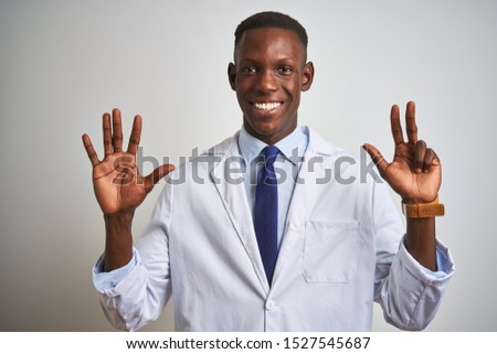 Young african american doctor man wearing coat standing over isolated white background showing and pointing up with fingers number eight while smiling confident and happy.