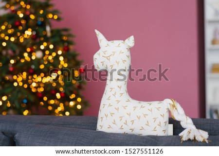 Handmade unicorn pillow on background of Christmas tree and lights