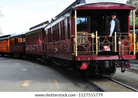 Caboose and unidentifiable conductor and red railroad cars standing in the train station. Royalty-Free Stock Photo #1527555779