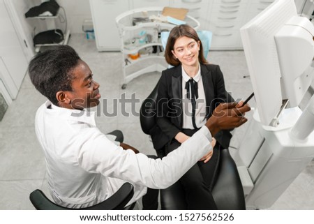 Young African male dentist shows x-rays on the monitor. Woman in the dentist chair at dental clinic. Medicine, health, stomatology concept. dentist treating a patient.